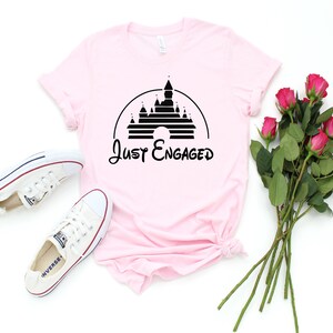 May include: Pink t-shirt with a black graphic of Cinderella's castle and the text "Just Engaged".