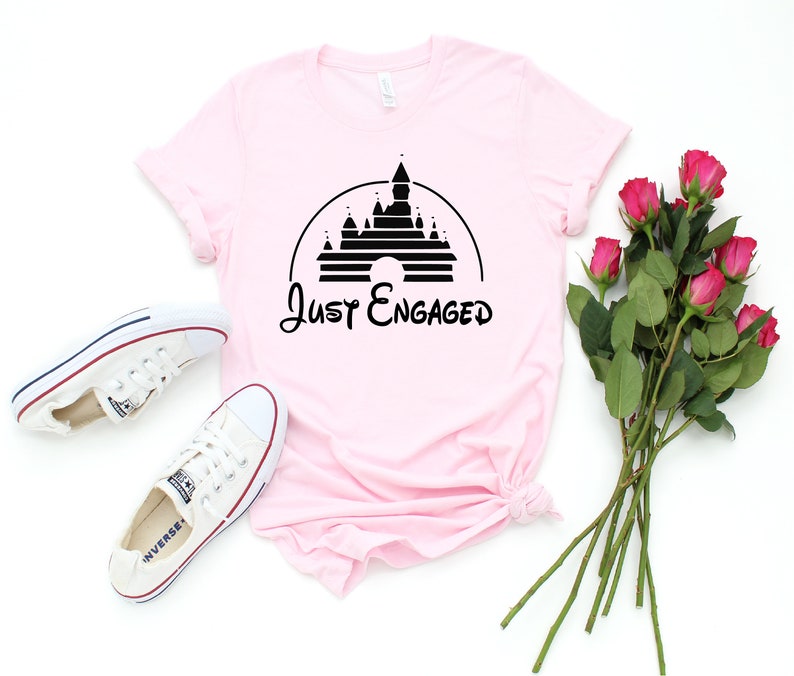 May include: Pink t-shirt with a black graphic of Cinderella's castle and the text "Just Engaged".