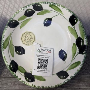 May include: A round ceramic bowl with a white base featuring a hand-painted pattern of dark olives and green leaves along the rim. A hexagonal sticker reads MADE IN ITALY ITALIE and a rectangular tag displays LA TAVOLA, MADE IN ITALY, and a QR code.