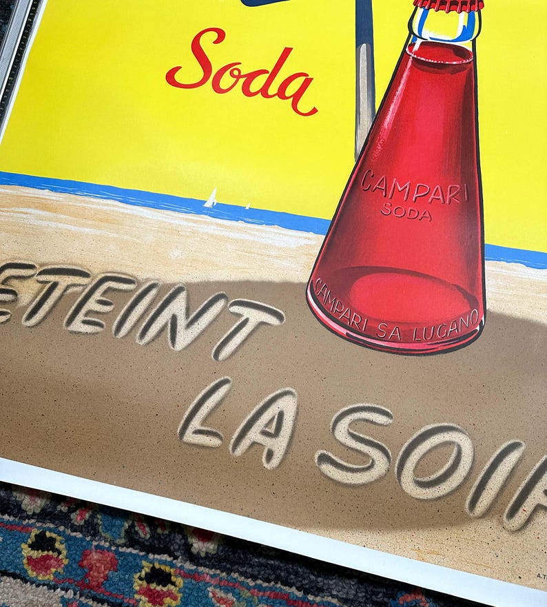 Pode incluir: Um an&uacute;ncio vintage de Campari Soda. A imagem apresenta uma garrafa de Campari Soda numa praia com as palavras "Eteint La Soif" escritas na areia. O fundo &eacute; amarelo brilhante com um oceano azul e veleiros brancos.