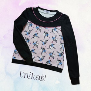 Könnte beinhalten: Schwarzer Langarm-Pullover mit einem rosafarbenen Einhorn-Druck und einem schwarzen und rosafarbenen Saum um den Halsausschnitt. Der Text "Unikat!" ist auf der Unterseite des Pullovers aufgedruckt.