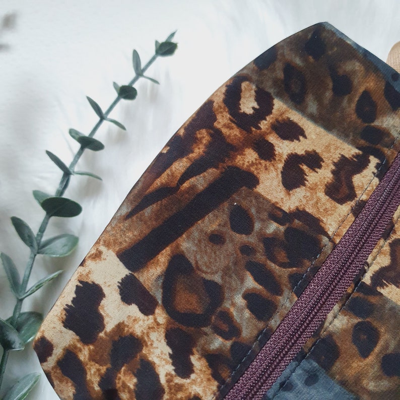 K&ouml;nnte beinhalten: Eine braune, beige und blaue Leopardenmuster-Clutch mit einem dunkelbraunen Rei&szlig;verschluss.