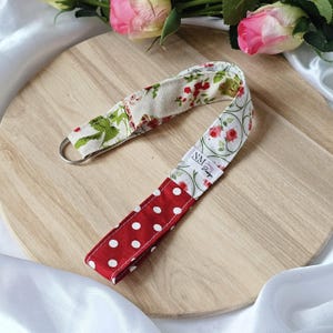 Könnte beinhalten: Ein Schlüsselband aus Stoff mit einem Metallring. Das Armband hat drei verschiedene Muster: rote Punkte, ein Blumendruck mit roten Rosen und cremefarbenem Stoff mit grünen Blättern und roten Blumen. Auf einer Holzoberfläche.