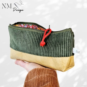 Könnte beinhalten: Handgemachte Federtasche mit grünem Cord-Oberteil und beigem Wildleder-Unterteil. Die Tasche hat einen roten Reißverschluss und ein bunt gemustertes Innenfutter. Der Markenname "NM Design" ist sichtbar.