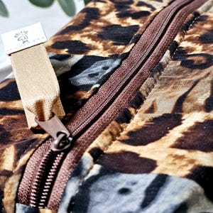 K&ouml;nnte beinhalten: Eine braune und beige gepunktete Rei&szlig;verschlusstasche mit einem braunen Rei&szlig;verschluss und einem beigefarbenen Stoffzugband. Die Tasche hat ein kleines wei&szlig;es Etikett mit dem Text "Blissful" und einem Symbol.