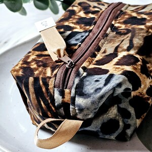 K&ouml;nnte beinhalten: Eine braune und beige Leopardenmuster-Rei&szlig;verschlusstasche mit einem beige Stoffgriff. Die Tasche hat einen braunen Rei&szlig;verschluss und ein kleines wei&szlig;es Etikett mit dem Text "Krafty Girl".