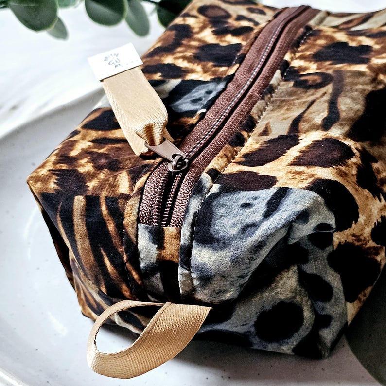 K&ouml;nnte beinhalten: Eine braune und beige Leopardenmuster-Rei&szlig;verschlusstasche mit einem beige Stoffgriff. Die Tasche hat einen braunen Rei&szlig;verschluss und ein kleines wei&szlig;es Etikett mit dem Text "Krafty Girl".