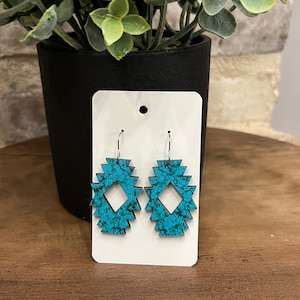 May include: A pair of turquoise blue earrings with a geometric design. The earrings are made of wood and have a silver hook.