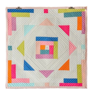 May include: A colorful quilt with a geometric pattern of squares and triangles in shades of pink, blue, green, orange, and yellow. The quilt is made of fabric with a white background and a subtle diagonal pattern.