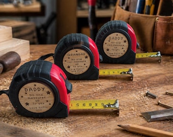 May include: Three black and red retractable tape measures with wooden circular inlays. Each inlay is engraved with text including Daddy or Grandad, the phrase No one measures up to you, star icons, and personalized names.