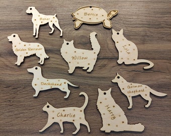May include: Wooden pet ornaments in various shapes, including a turtle, cats, and dogs. Each ornament is engraved with a pet's name and star details. Names include Bertie, Boxer, Willow, Dachshund, Charlie, Harry, Lola, and German shepherd.