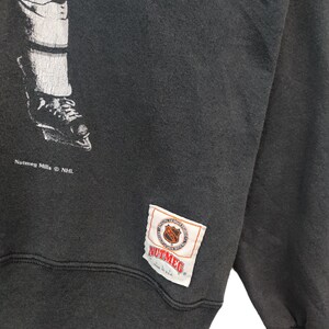 K&ouml;nnte beinhalten: Dunkelgraues Vintage-Sweatshirt mit einer schwarz-wei&szlig;en Grafik eines Hockey-Spielerbeins und -schlittschuhs. Das Sweatshirt hat ein Nutmeg Mills NHL-Etikett.