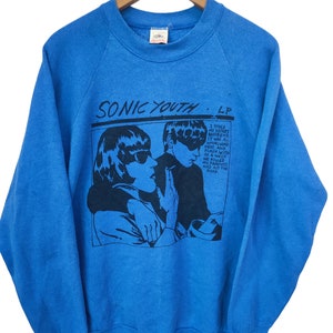 Pode incluir: Camisola azul com um gráfico a preto e branco de duas figuras com óculos de sol e o texto "SONIC YOUTH LP". O gráfico inclui o texto "I stole my sister's boyfriend..." no lado direito.