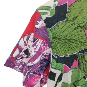 Może przedstawiać: Zbliżenie koszulki z kr&oacute;tkim rękawem z żywym kwiatowym wzorem. Projekt zawiera duże zielone liście, r&oacute;żowe i fioletowe kwiaty oraz czerwone akcenty. Tkanina wydaje się być lekkim materiałem.