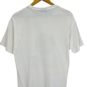 May include: A plain white t-shirt hanging on a wooden hanger. The short-sleeved shirt is made of a soft material and is displayed against a white background. The shirt is a basic, versatile garment.