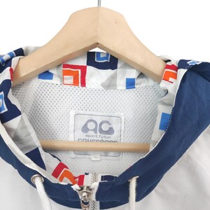 May include: White and navy blue hooded jacket with a geometric pattern on the hood lining. The jacket features a full zipper, drawstring, and a label with the text "sport futur collection". The jacket is hanging on a wooden hanger.