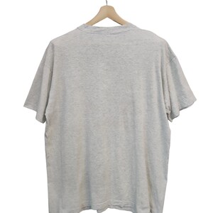 May include: A heather gray t-shirt hanging on a wooden hanger. The short-sleeved shirt is made of a soft material and has a crew neck. The back of the shirt is visible.