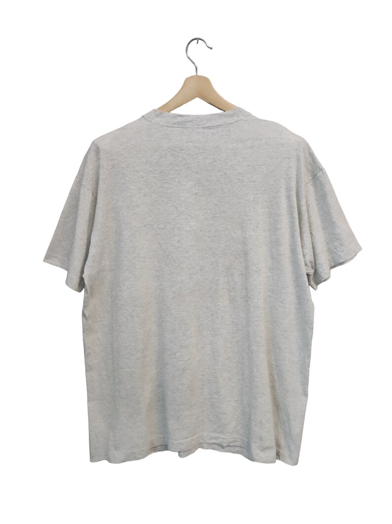 May include: A heather gray t-shirt hanging on a wooden hanger. The short-sleeved shirt is made of a soft material and has a crew neck. The back of the shirt is visible.