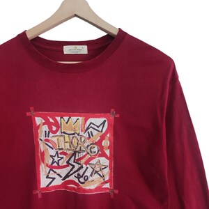 Puede incluir: Camiseta burdeos de manga larga con un dise&ntilde;o gr&aacute;fico. El dise&ntilde;o presenta una corona, estrellas y la palabra "THOR" en una est&eacute;tica de graffiti, enmarcada por un borde rojo. La camiseta est&aacute; colgada en una percha de madera.