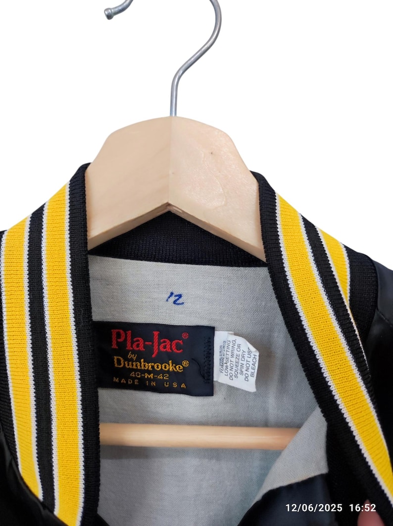 May include: Black and yellow varsity jacket with a black collar and yellow stripes. The jacket is hanging on a wooden hanger. The label reads "Pla-Jac by Dunbrooke" and "Made in USA".
