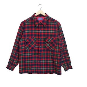 May include: A red, green, and navy blue plaid flannel shirt with long sleeves and two chest pockets. The shirt is button-down and hangs from a wooden hanger. The collar and cuffs are visible.