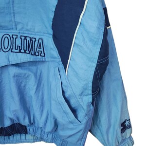 May include: A light blue and navy blue pullover windbreaker jacket featuring the text OLINA embroidered in navy blue on the front pocket flap. The jacket includes a side zip, elastic cuffs, and a Starter logo patch on the left sleeve.