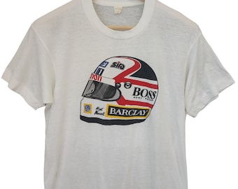 May include: White t-shirt featuring a graphic of a racing helmet. The helmet design includes red, black, and white accents, with the "BOSS" and "BARCLAY" logos prominently displayed. The shirt is hanging on a wooden hanger.