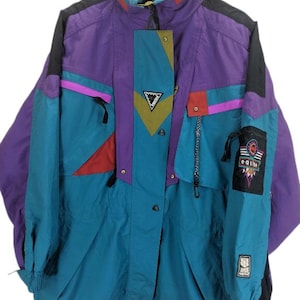 May include: A retro ski jacket in teal, purple, and black. The jacket has a high collar, multiple pockets, and a colour-blocked design with red and pink accents. The jacket has the word "eque" on the sleeve.