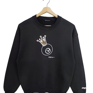 Puede incluir: Sudadera negra con un diseño gráfico de una bola de billar coronada. La corona es dorada y la bola es blanca con un contorno negro. El texto "eight" está en la manga derecha.