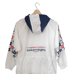 May include: White jacket with a navy blue hood and trim, featuring a drawstring waist and long sleeves. The jacket has a geometric pattern in red, blue, and gray on the sleeves. The text "sport futur courr&egrave;ges paris" is printed on the back.