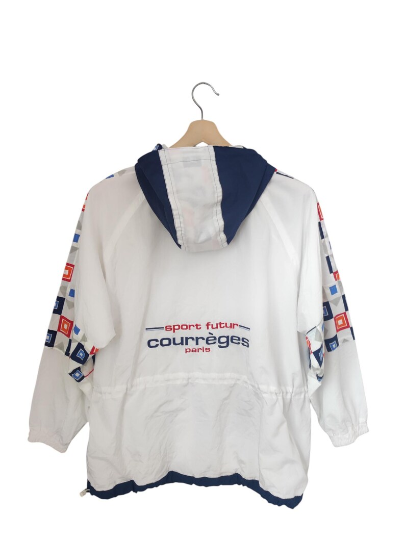 May include: White jacket with a navy blue hood and trim, featuring a drawstring waist and long sleeves. The jacket has a geometric pattern in red, blue, and gray on the sleeves. The text "sport futur courr&egrave;ges paris" is printed on the back.