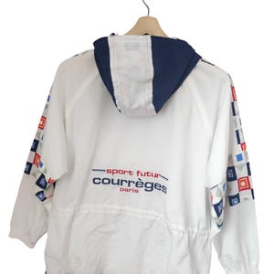May include: White jacket with a navy blue hood and trim, featuring a drawstring waist and geometric patterns on the sleeves. The jacket has the text "sport futur courr&egrave;ges paris" in red and blue.