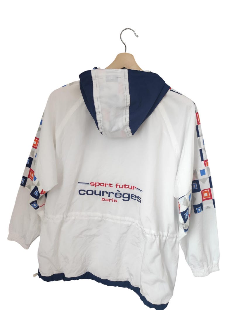 May include: White jacket with a navy blue hood and trim, featuring a drawstring waist and geometric patterns on the sleeves. The jacket has the text "sport futur courr&egrave;ges paris" in red and blue.
