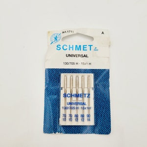 Op de afbeelding: Een verpakking met vijf zilveren naalden voor naaimachines, met het label "Schmetz Universal 130/705 H 15x1 H". De verpakking is blauw en wit met een witte achtergrond en blauwe tekst.