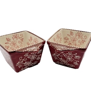 Könnte beinhalten: Zwei bordeauxfarbene quadratische Keramikschalen mit floralen Mustern. Die Schalen haben eine cremefarbene Innenseite mit einem floralen Muster und einem dekorativen Rand. Die Außenseite weist weiße Blumenmuster auf.