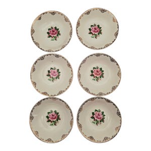 May include: Six cream-colored bowls with a pink rose in the center. The bowls have a gold-colored decorative trim around the rim. The bowls are arranged in two rows of three.