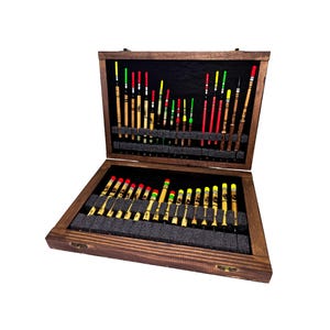 May include: An open wooden box, stained dark, containing a selection of fishing floats. The floats are in various colours, including red, green, and yellow, and are arranged in rows within the box.