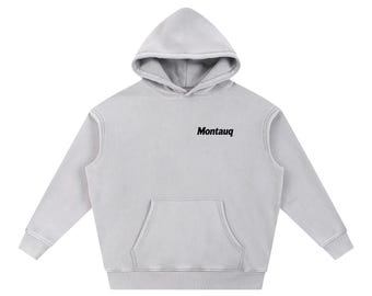 May include: A light gray hoodie with a front pocket and a hood. The word "Montauq" is printed in black on the chest. The hoodie has long sleeves and a relaxed fit.