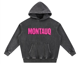 May include: A charcoal gray hoodie with a front pocket and a hood. The word "MONTAUQ" is printed across the chest in bright pink letters. The hoodie has long sleeves and a relaxed fit.