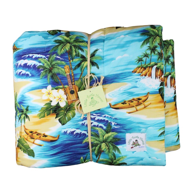 Puede incluir: Una colcha de tem&aacute;tica hawaiana azul y amarilla con palmeras, olas y un ukelele. La colcha est&aacute; atada con cuerda y tiene una etiqueta que dice "Little Turtle Heaven".