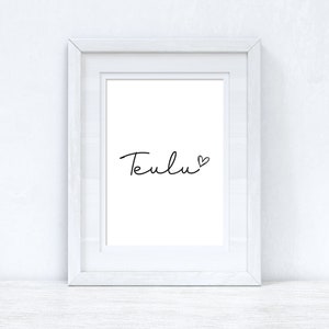 Könnte beinhalten: Weißer Bilderrahmen mit einem weißen Passepartout und einem Schwarzweißdruck mit der Aufschrift "Teulu" mit einem kleinen Herzsymbol.