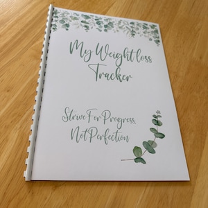 May include: A white spiral bound journal with a green leafy design and the text "My Weight Loss Tracker" and "Strive For Progress, Not Perfection".