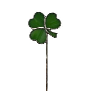May include: A silver pin with a green shamrock design. The shamrock is made of glass and has a white center.