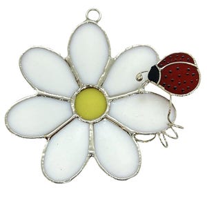 May include: A stained glass daisy with a yellow center and a red ladybug on one of the petals.