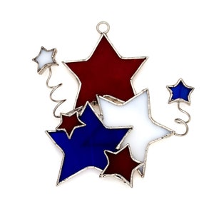 May include: A stained glass ornament featuring five stars in red, white, and blue. The stars are connected by a silver wire, creating a whimsical design.