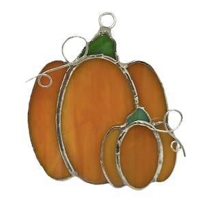 May include: A stained glass ornament featuring three pumpkins in shades of orange and green. The pumpkins are connected by wire loops, creating a whimsical design.