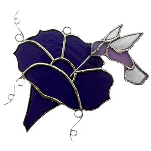 May include: A stained glass hummingbird with purple and white wings, feeding from a purple flower.