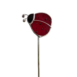May include: A red and black ladybug garden stake with a silver metal stem. The ladybug has a red body with black spots and a black head. The antennae are silver and curved.