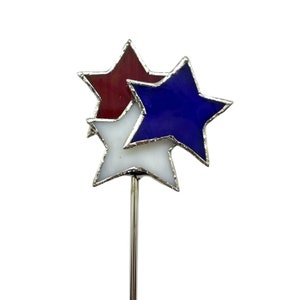 May include: A decorative star-shaped garden stake featuring three stars in red, white, and blue. The stars are made of stained glass and are arranged in a cluster. The stake is made of silver metal.