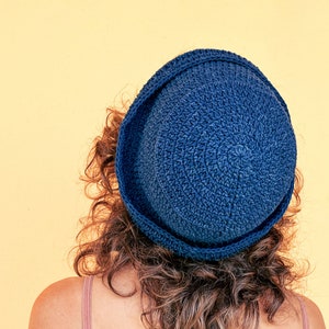 May include: A person wearing a blue crocheted hat. The hat has a wide brim and is made of a thick yarn.